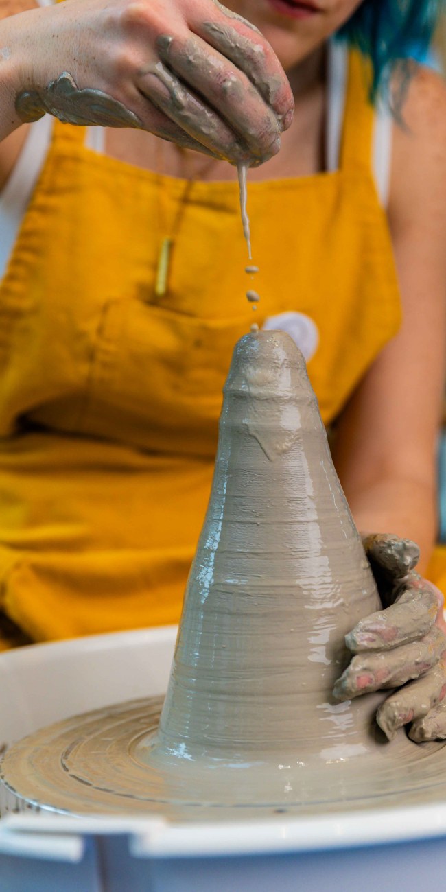 A close-up of a women throwing pottery on the wheel, centering a piece of clay and dripping water on top of it, in a pottery workshop at Zolta Ceramics Studio