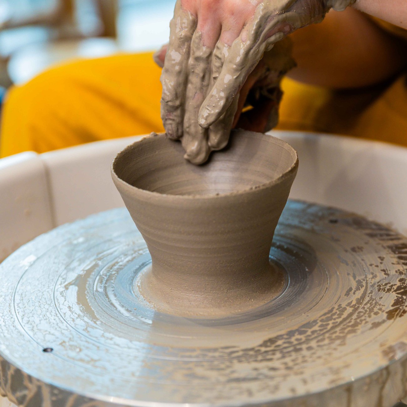 a close-up on a woman throwing a small coin pot on the pottery wheel at Zolta Ceramics Studio