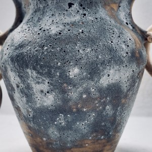 A ceramic vessel by Sirin AlMasri titled Nawah, with a cratered exterior, glossy turquoise interior, and sculptural ceramic chains on both sides. Inspired by the Earth's core, the piece explores density, tension, and elemental presence through clay and glaze.