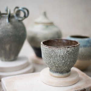 Handcrafted ceramic art piece titled “The Summoning” by Sirin AlMasri in Zolta Studio, featuring five sculptural loop handles and a textured volcanic glaze in deep green, blue, and charcoal tones. Modern interpretation of ritual pottery with oxidized copper surface effects.