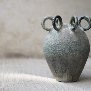 Handcrafted ceramic art piece titled “The Summoning” by Sirin AlMasri in Zolta Studio, featuring five sculptural loop handles and a textured volcanic glaze in deep green, blue, and charcoal tones. Modern interpretation of ritual pottery with oxidized copper surface effects.